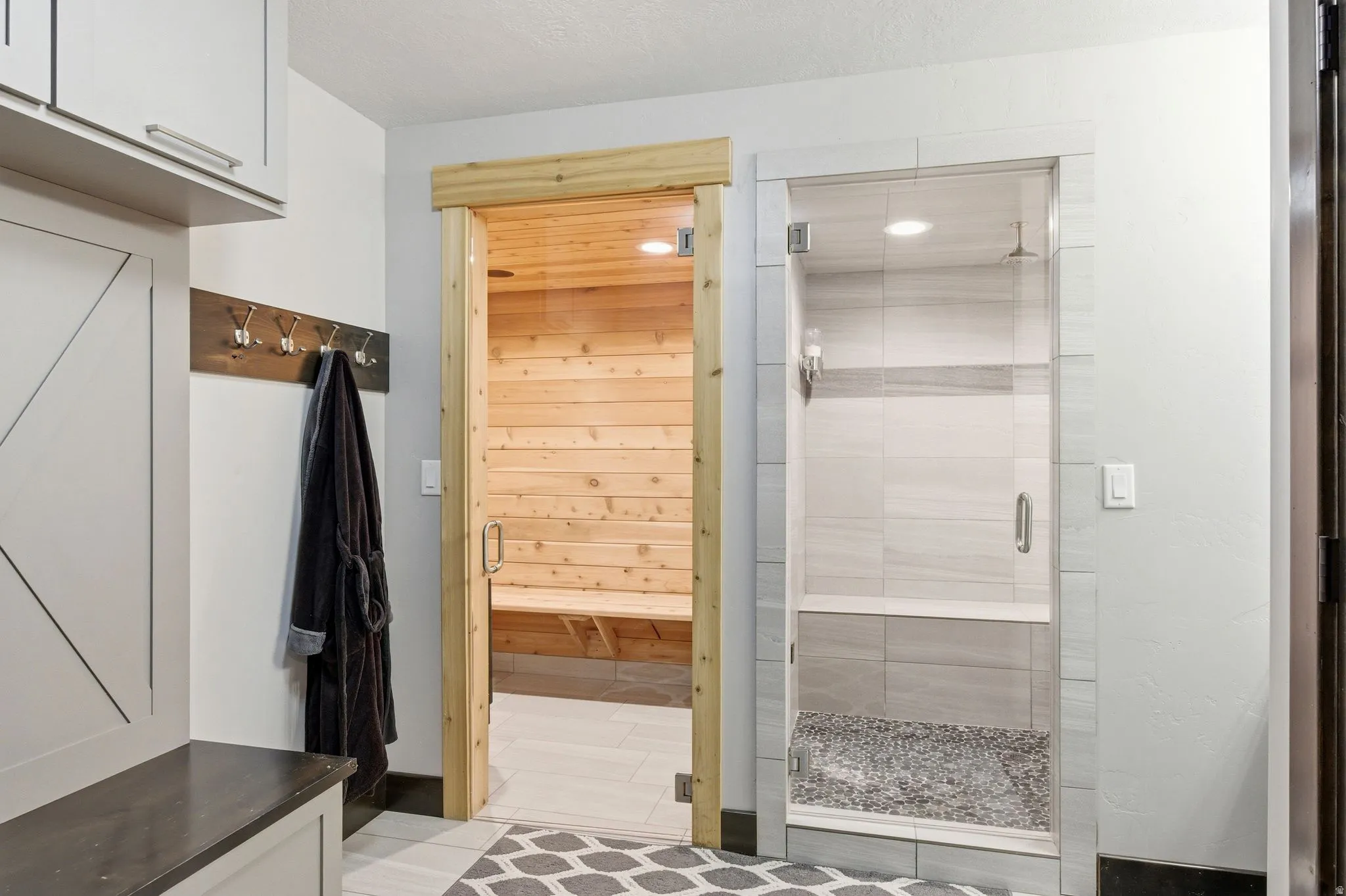 Spa-inspired amenities with a wood-lined sauna and a glass-enclosed shower featuring a tiled bench and pebble floor