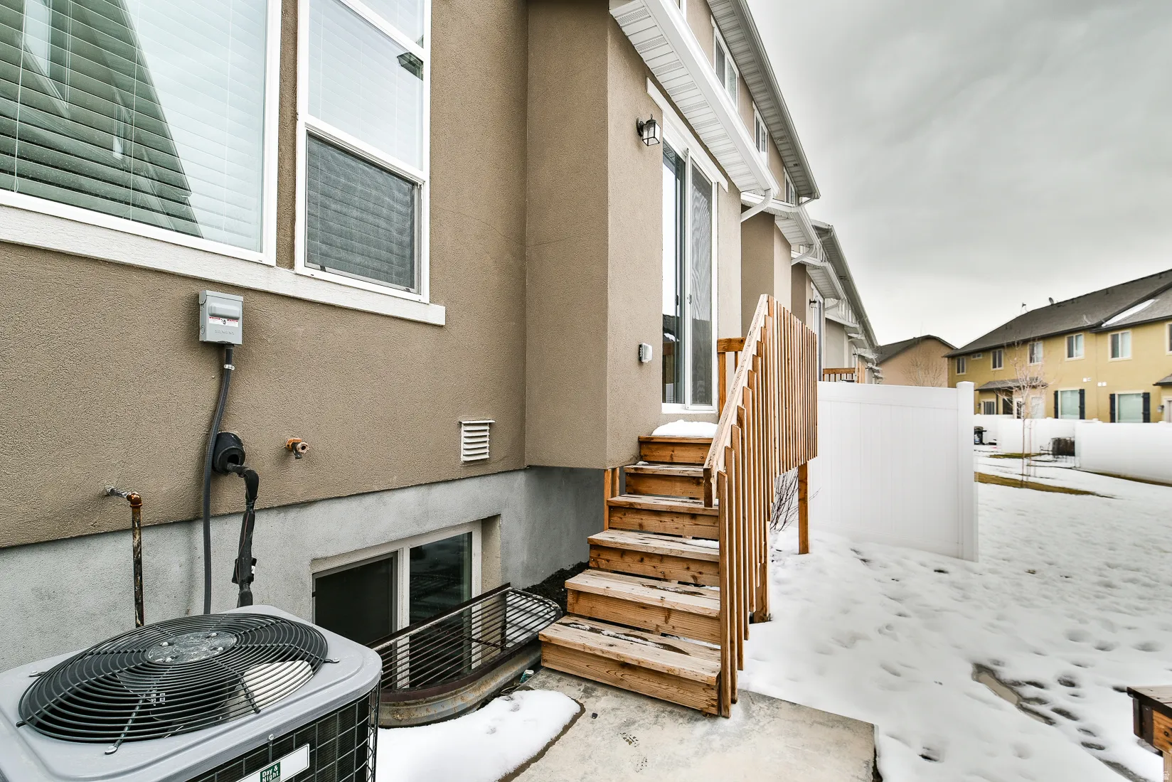 Rear exterior featuring a sliding glass door, wooden deck stairs, a window well, and a white privacy fence