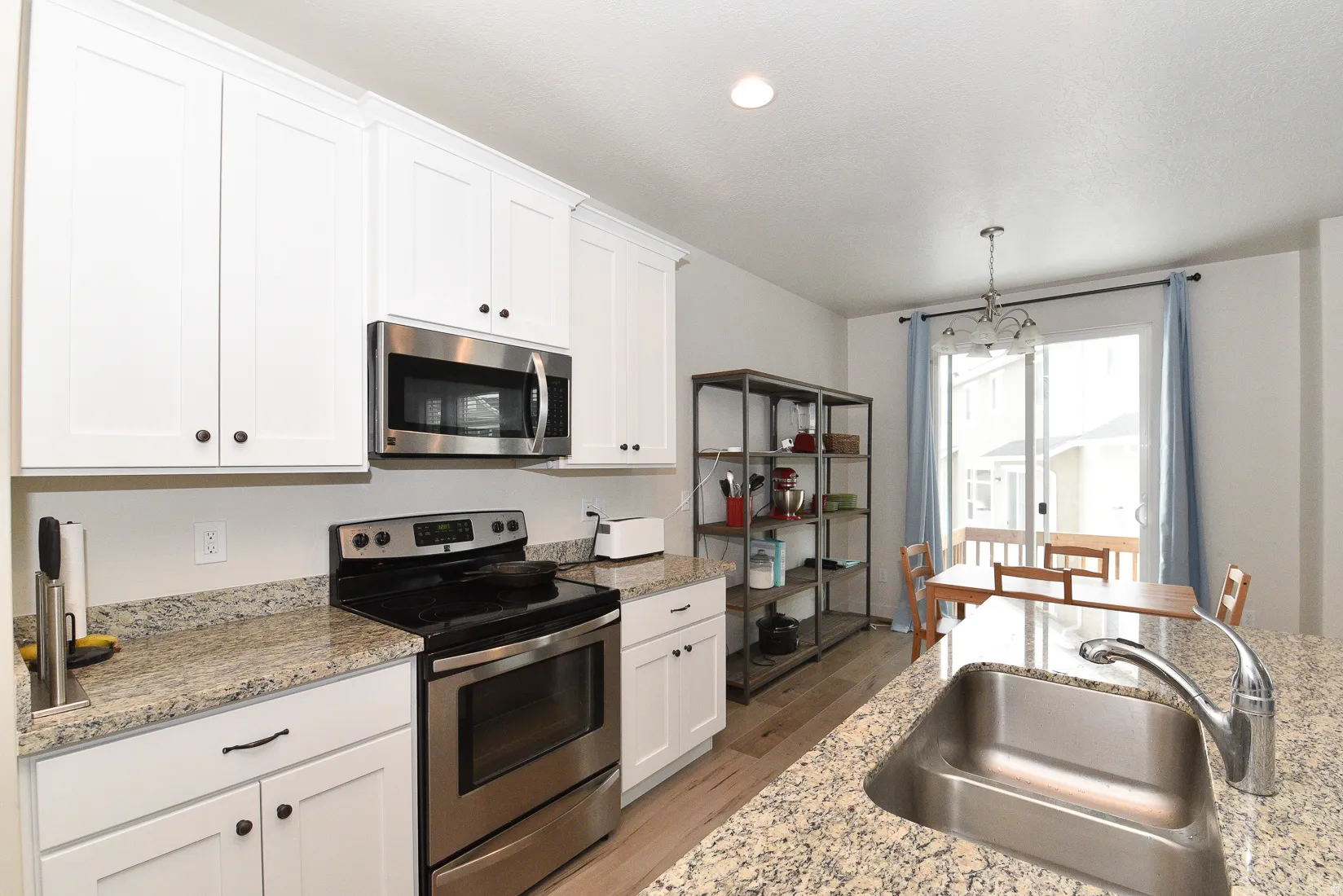 Kitchen featuring white cabinetry, stainless steel appliances, granite countertops, wood-finish flooring, and a sliding glass door