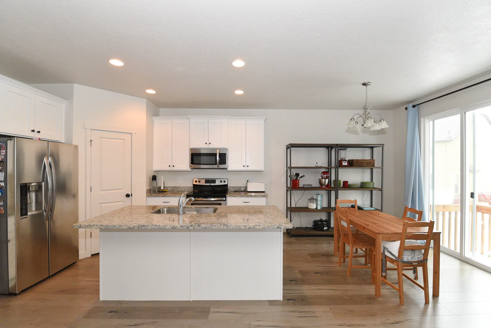 Modern kitchen featuring a central island with a light-toned granite countertop, under-mount stainless steel sink, and white cabinetry