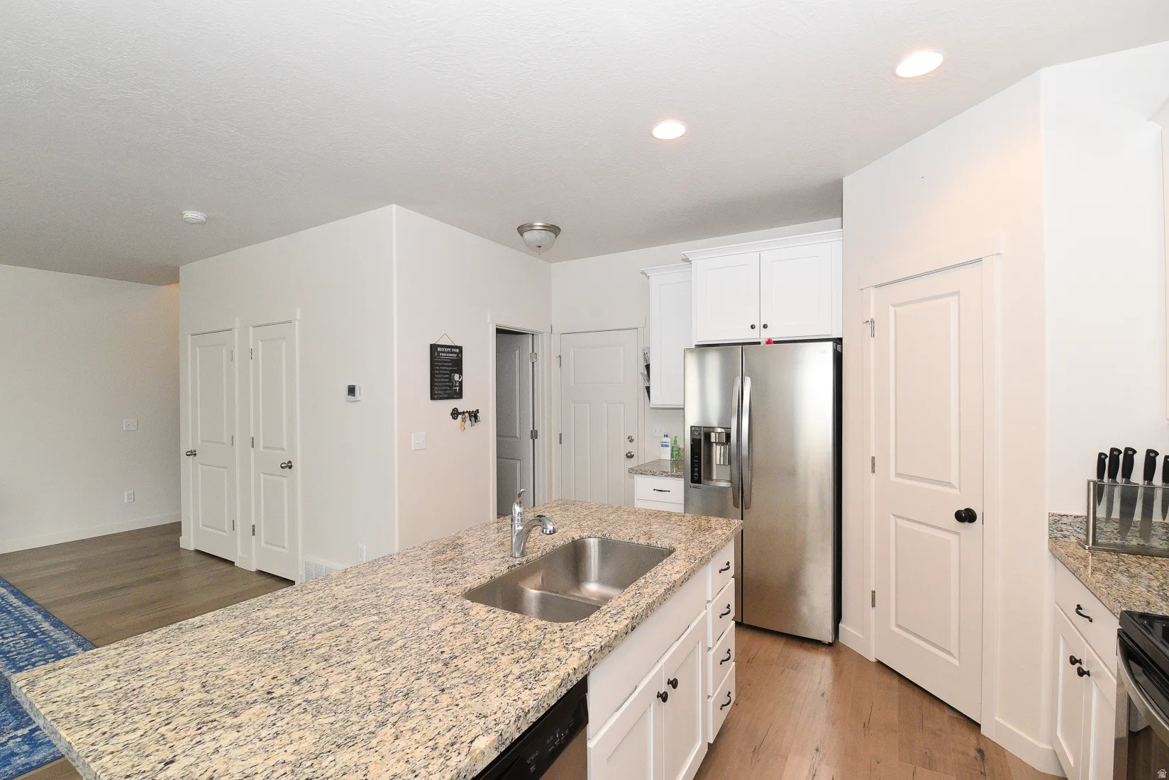 Kitchen featuring a central island with dual basin sink, granite countertops, white cabinetry, stainless steel appliances, and wood-finish flooring