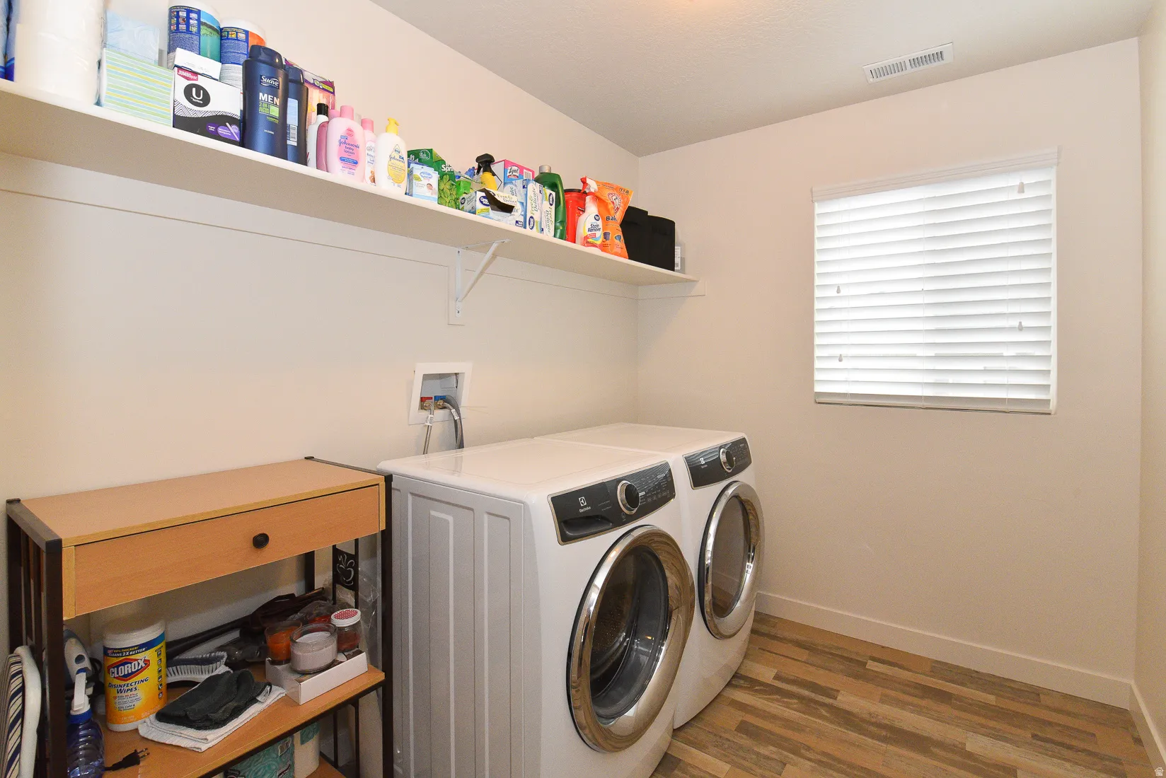 Dedicated laundry space featuring wood-finish flooring and a window with blinds