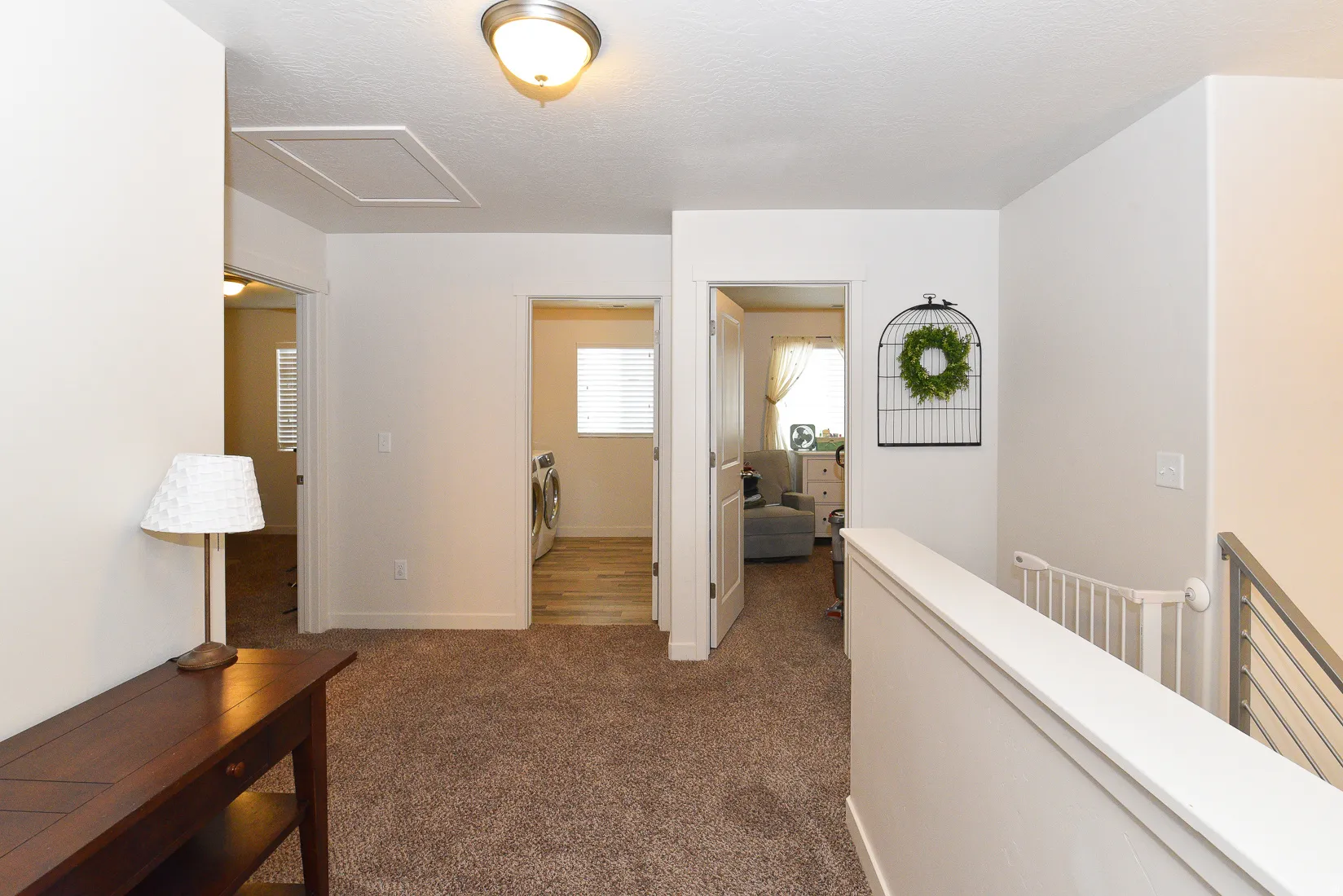 Upper-level hallway featuring plush carpeting, a ceiling-mounted light fixture, white interior doors, and a staircase with a horizontal metal railing