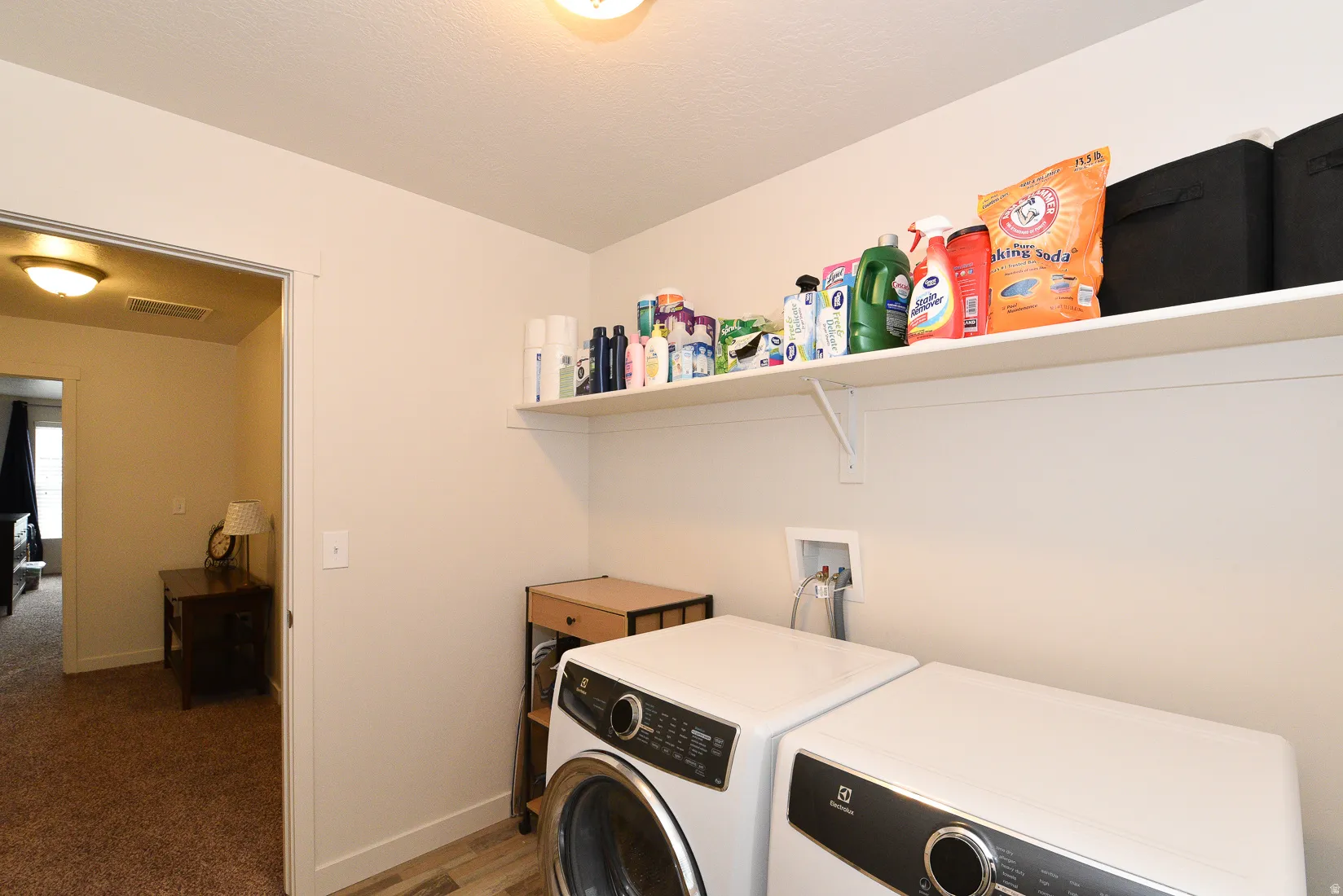 Dedicated laundry area featuring a wall-mounted shelf, light-toned wall paint, and wood-finish flooring