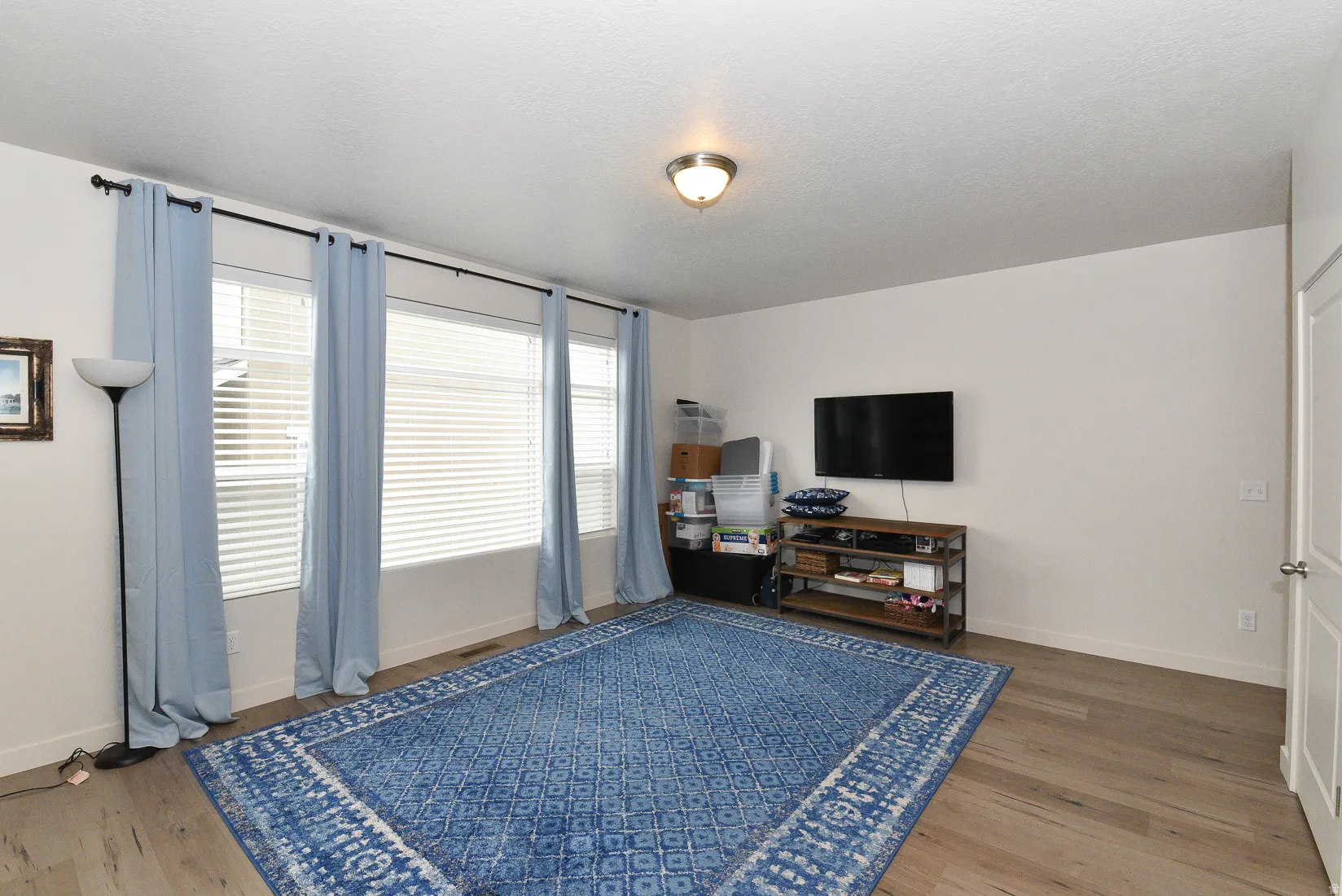 Spacious room featuring wood-finish flooring, white walls, and a series of three windows with horizontal blinds