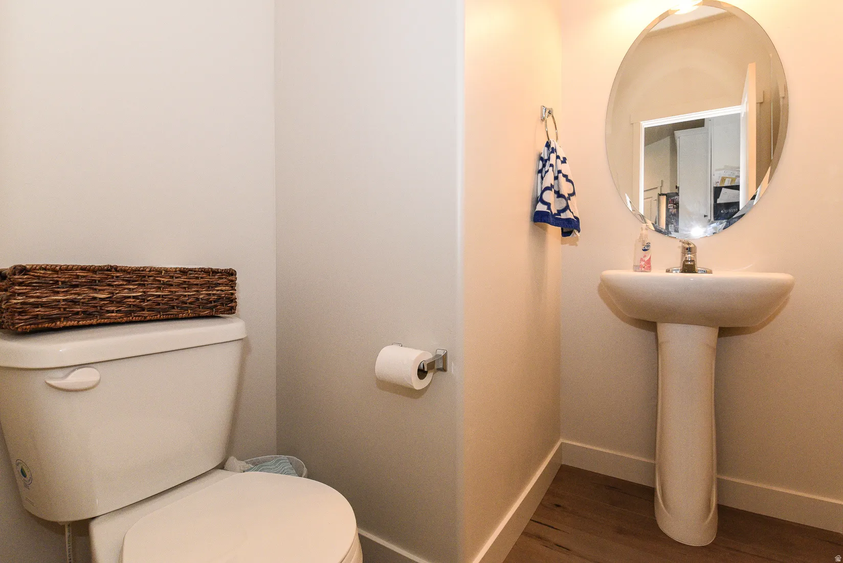Pedestal sink with an oval mirror and wood-finish flooring