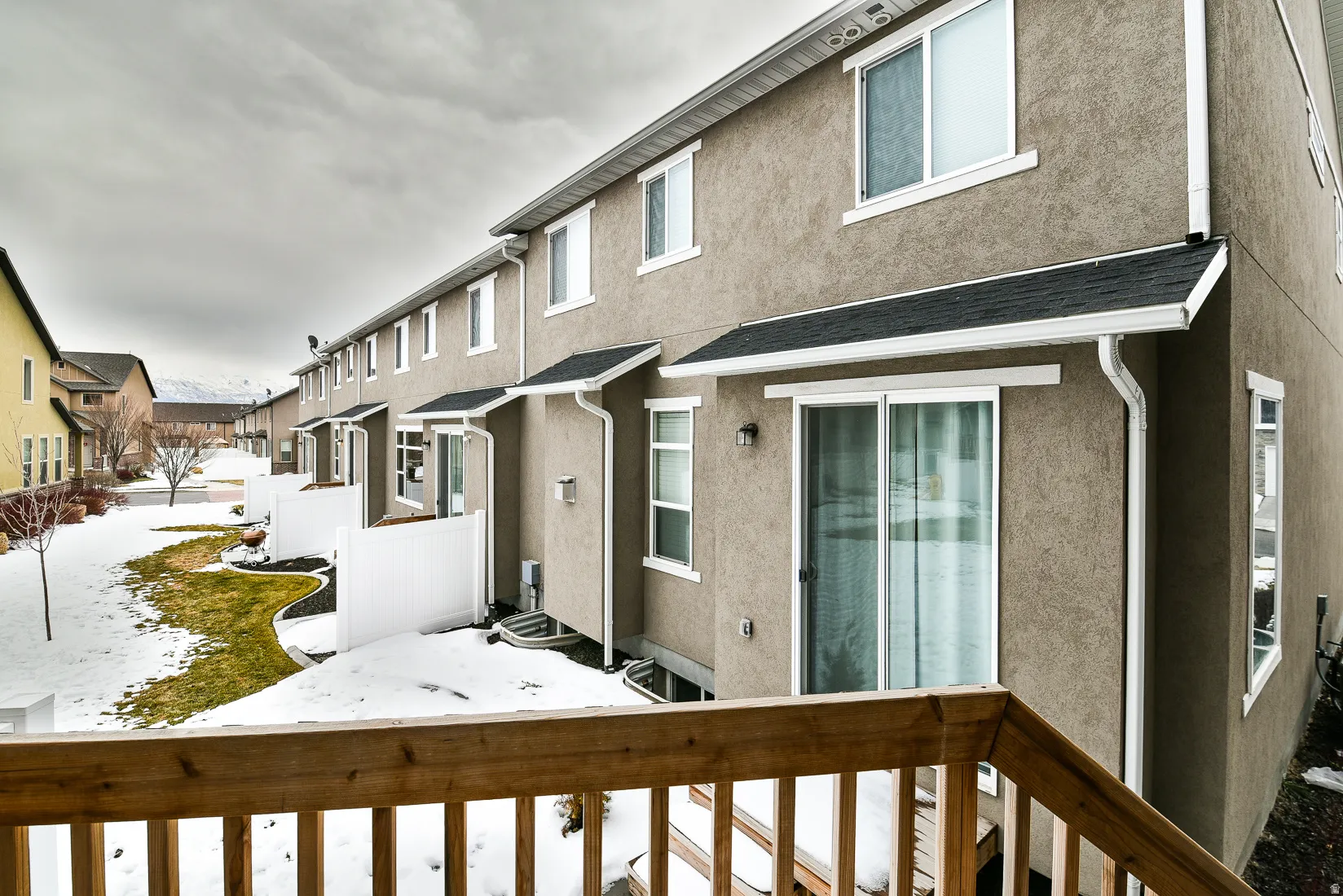 Rear exterior featuring stucco finish, multiple sliding glass doors, white vinyl fencing, and a wooden deck railing