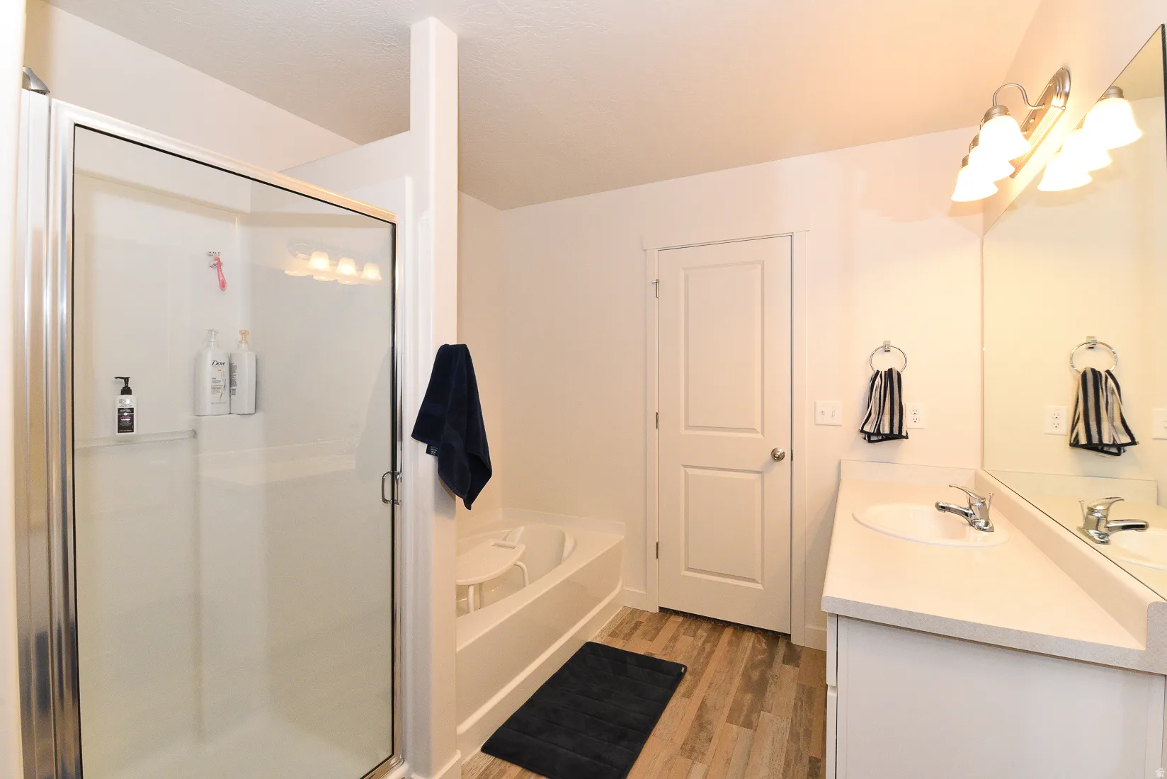 Bathroom featuring a glass-enclosed shower, a separate bathtub, a single vanity with an integrated sink and countertop, a large wall-mounted mirror, and wood-finish flooring