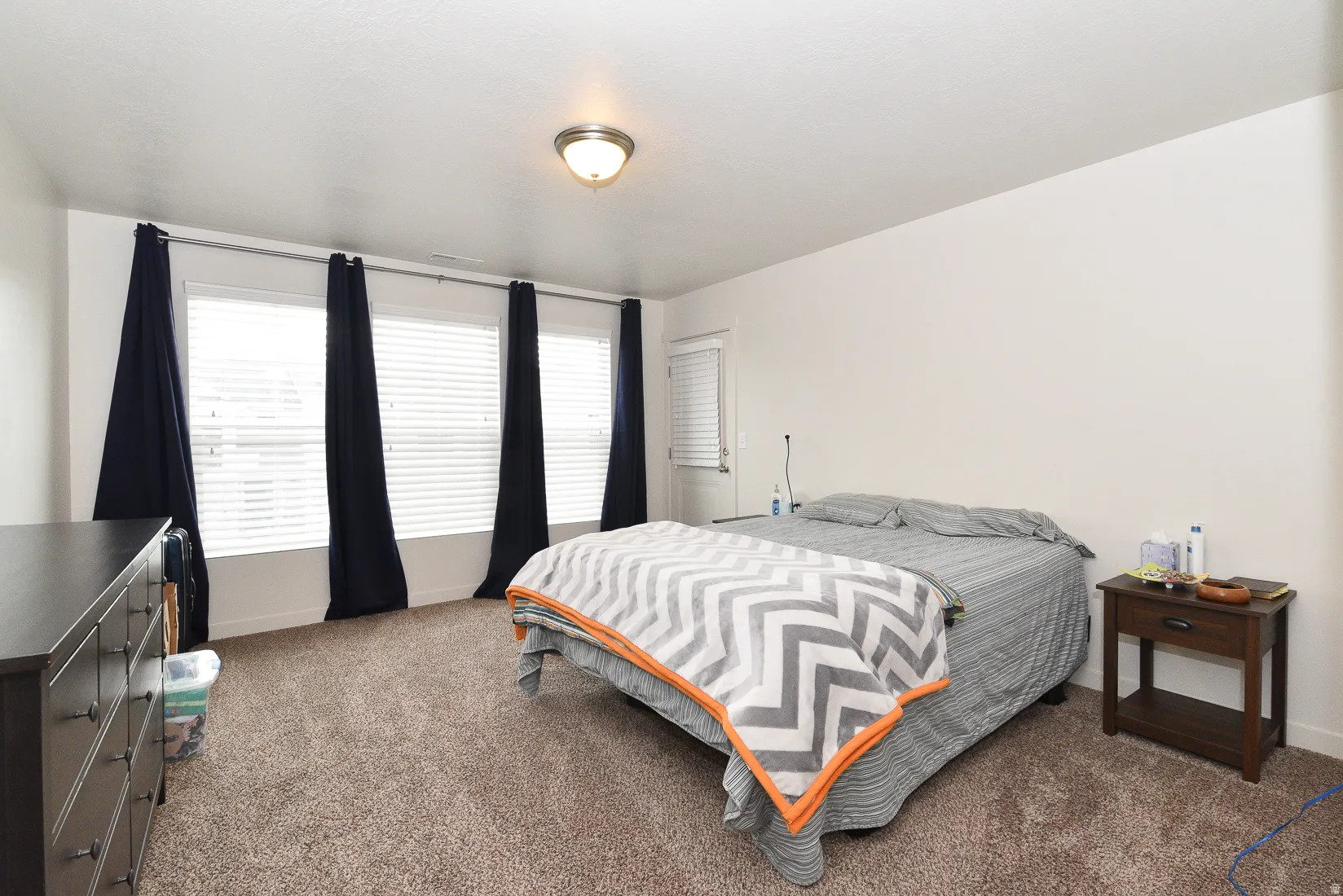 Spacious room featuring multiple windows with blinds, a neutral wall color, and textured carpeting