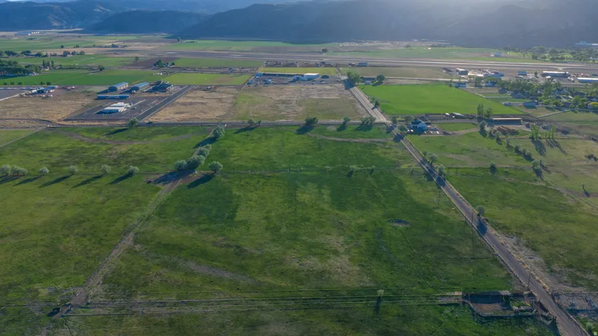 Expansive agricultural land featuring a verdant field, mountain backdrop, and multiple access roads