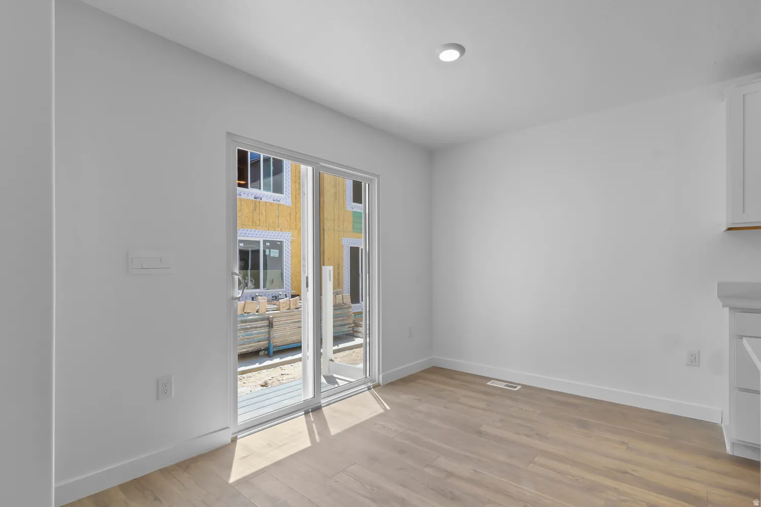 Sliding glass door opening to an exterior area, featuring wood-finish flooring, white walls, and a recessed ceiling light