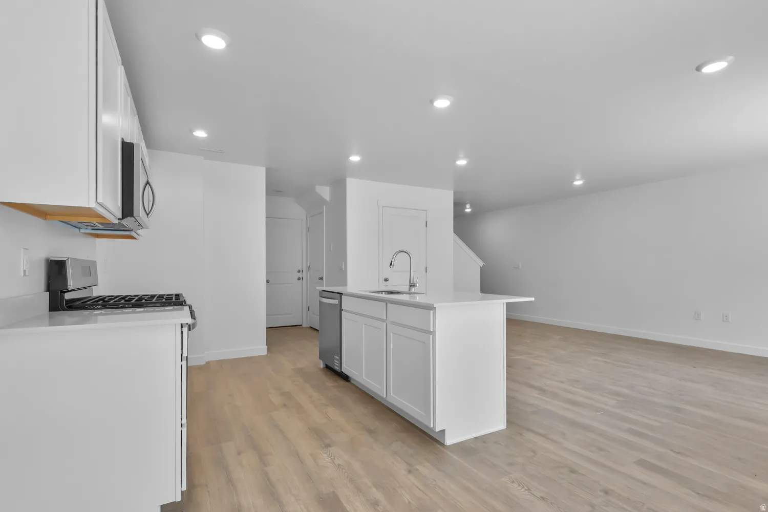 Open-concept living space with light wood-finish flooring, recessed lighting, and white walls
