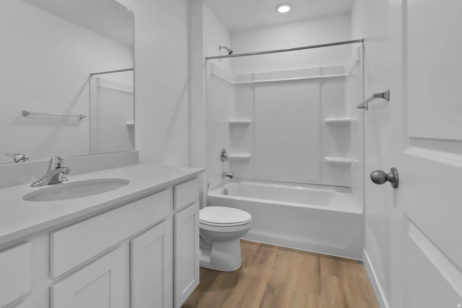 Bathroom featuring a single vanity with an undermount sink, a large mirror, a shower-tub combination with a white surround, and wood-finish flooring