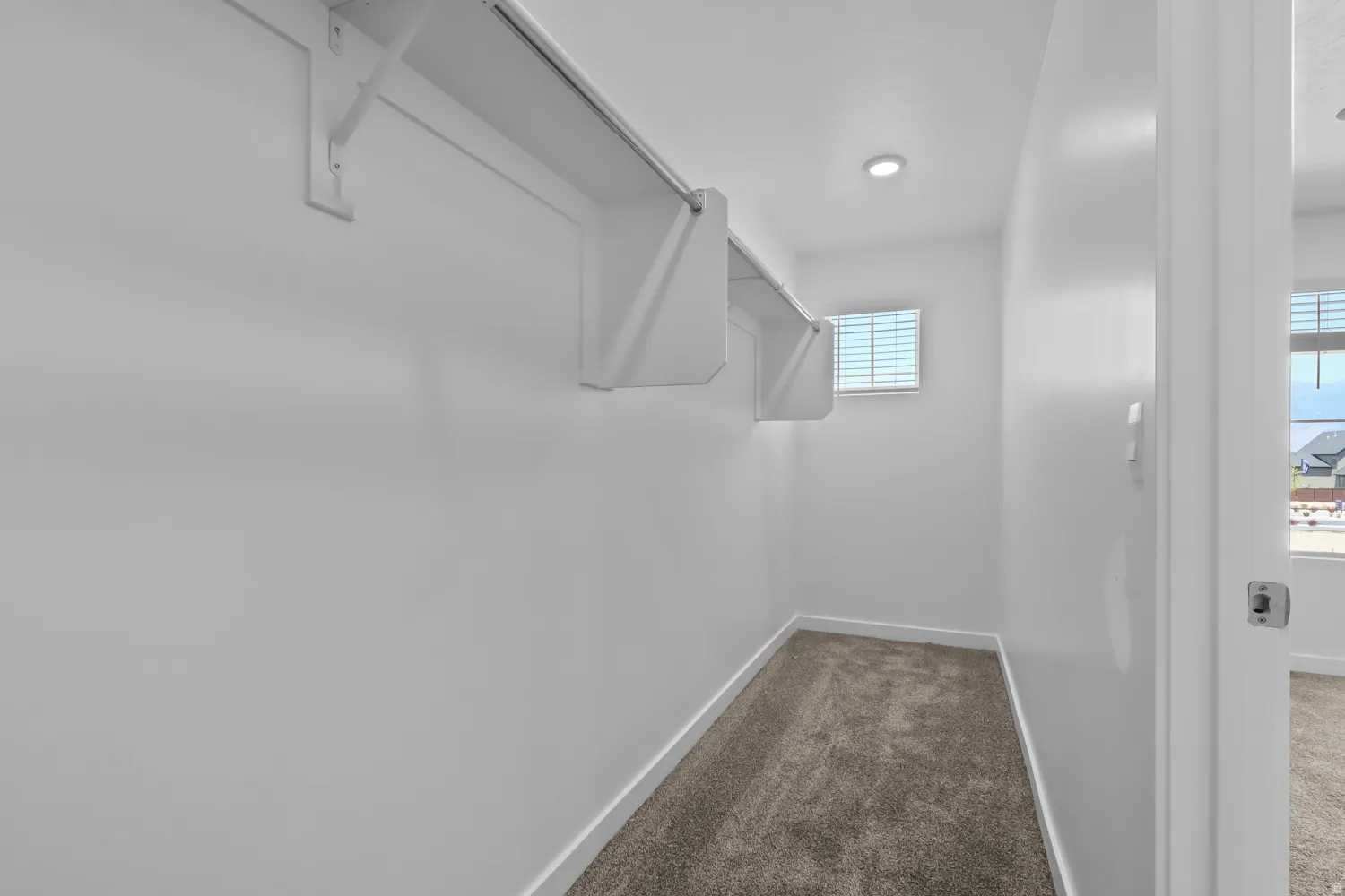Bright closet space featuring built-in shelving, a hanging rod, recessed lighting, and a window with blinds