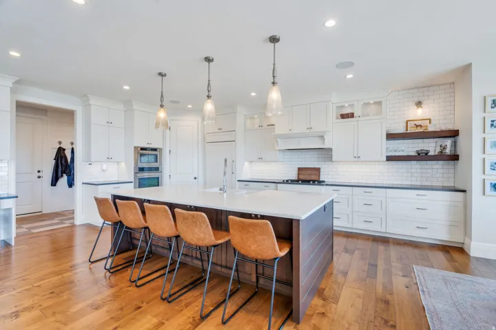 Spacious kitchen featuring a large central island with seating, white cabinetry, dark countertops, and a subway tile backsplash