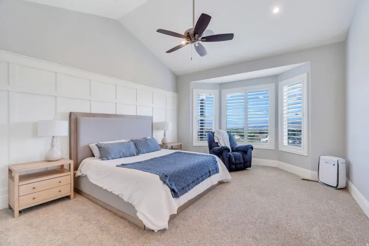 Bedroom featuring a vaulted ceiling with a ceiling fan, a board and batten accent wall, and plush carpeting