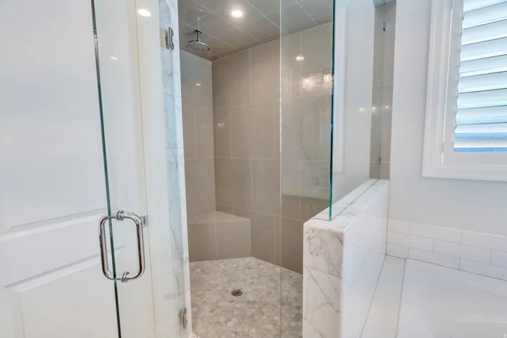Glass-enclosed shower featuring a rain showerhead, built-in bench, and mosaic tile flooring