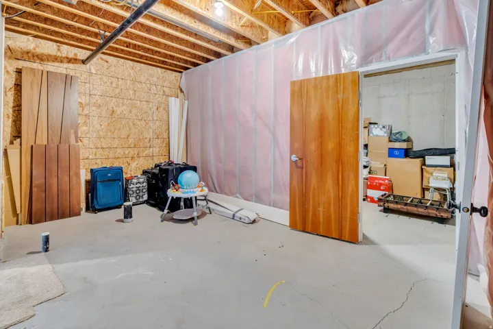 Unfinished basement area featuring exposed ceiling joists, concrete flooring, and a wood-paneled door