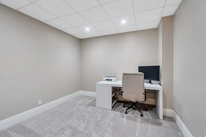 Room featuring textured carpet flooring, neutral wall tones, white baseboards, and a grid panel ceiling with recessed lighting