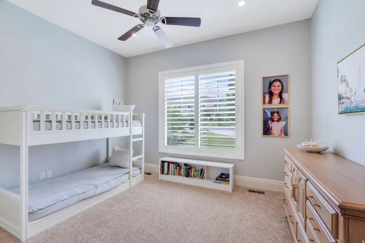 Bright room featuring a large window with white plantation shutters, neutral carpeting, a ceiling fan, recessed lighting, and a built-in bookshelf