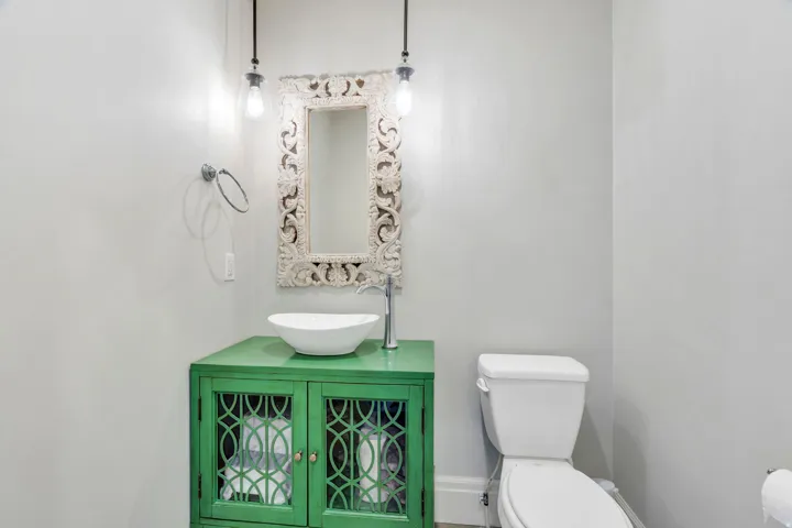 Powder room featuring a green vanity with decorative cabinet doors, a vessel sink, and a carved ornate mirror