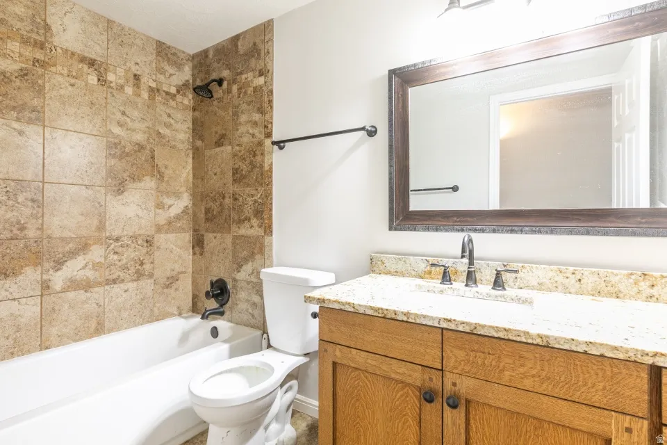 Bathroom featuring a full tub with tiled surround, a vanity with wood-finish cabinetry, a light-toned countertop, and an oversized mirror