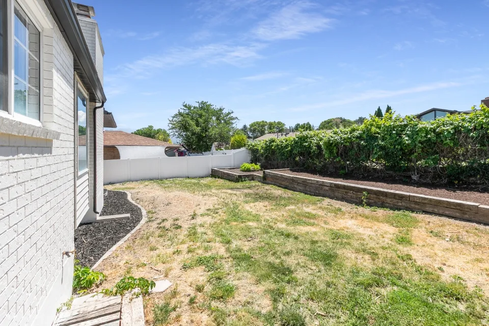 Fenced backyard with raised garden beds and a white brick exterior