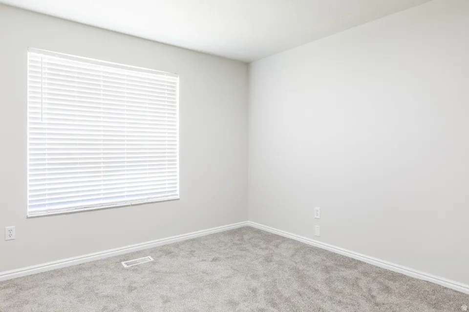 Neutral-toned room featuring a single window with horizontal blinds, light gray wall paint, white trim, and gray carpet flooring