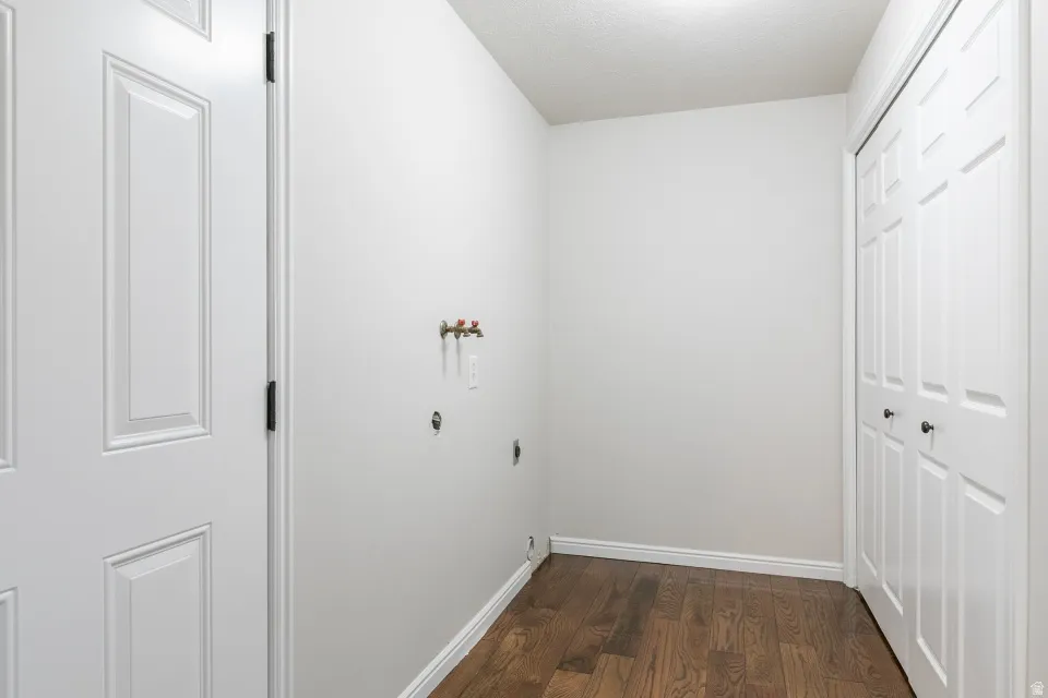 Dedicated laundry area featuring hookups, dark wood-finish flooring, white baseboards, and bi-fold doors