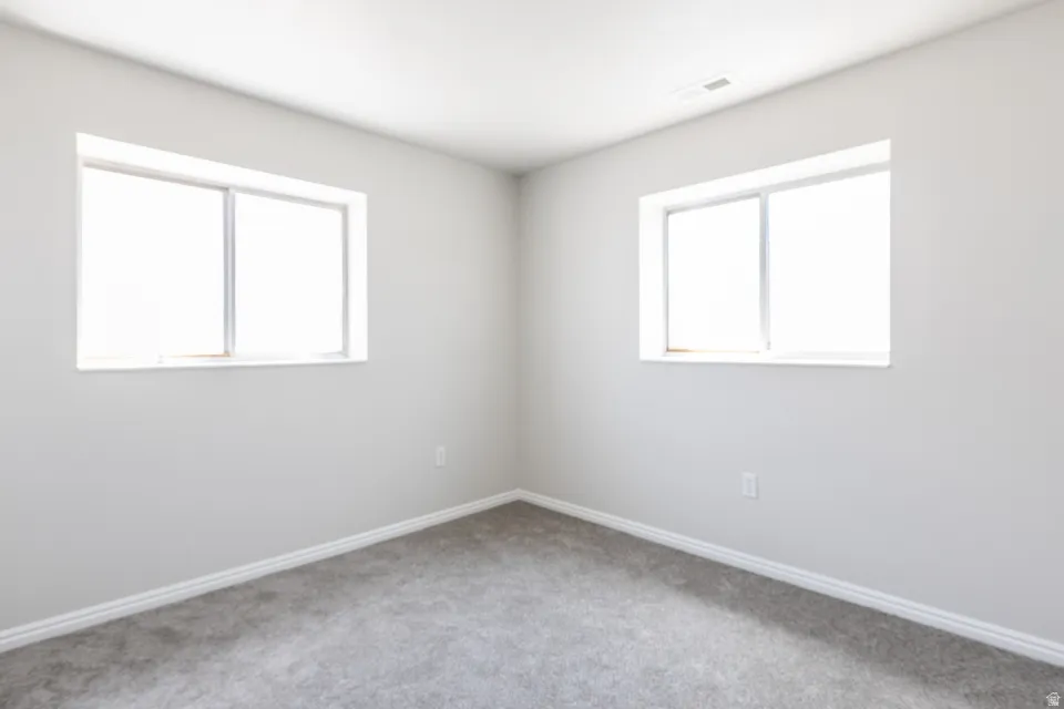 Bright interior space featuring two windows, light gray wall paint, and gray carpeting