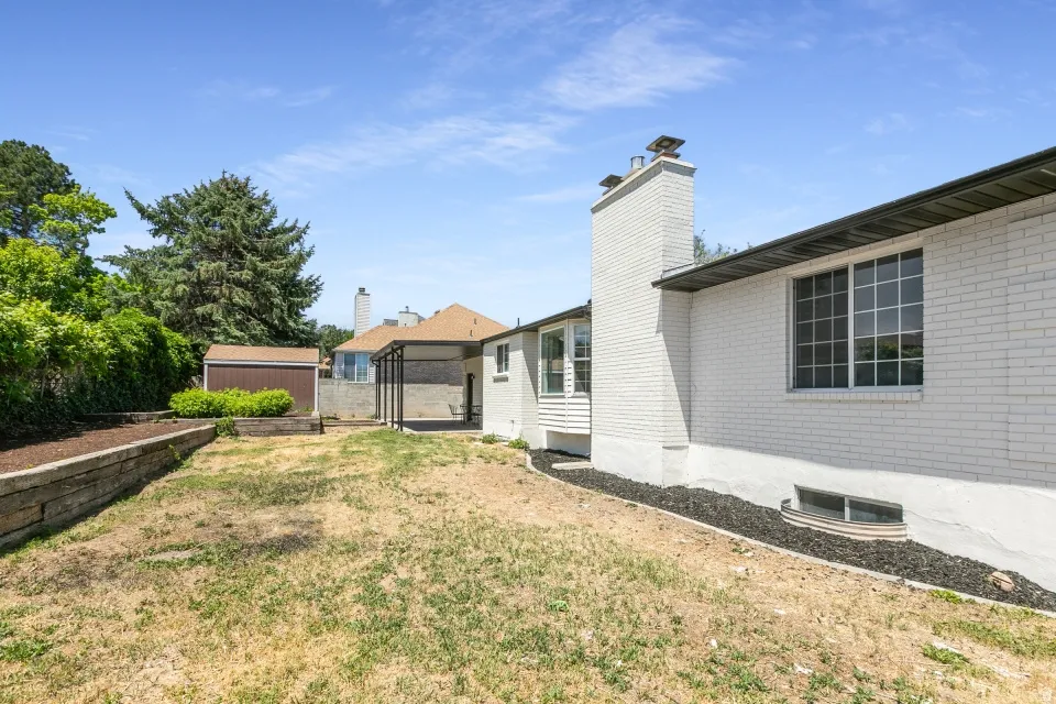 Spacious rear yard featuring a detached storage shed, a covered patio area, and a brick exterior with multiple windows