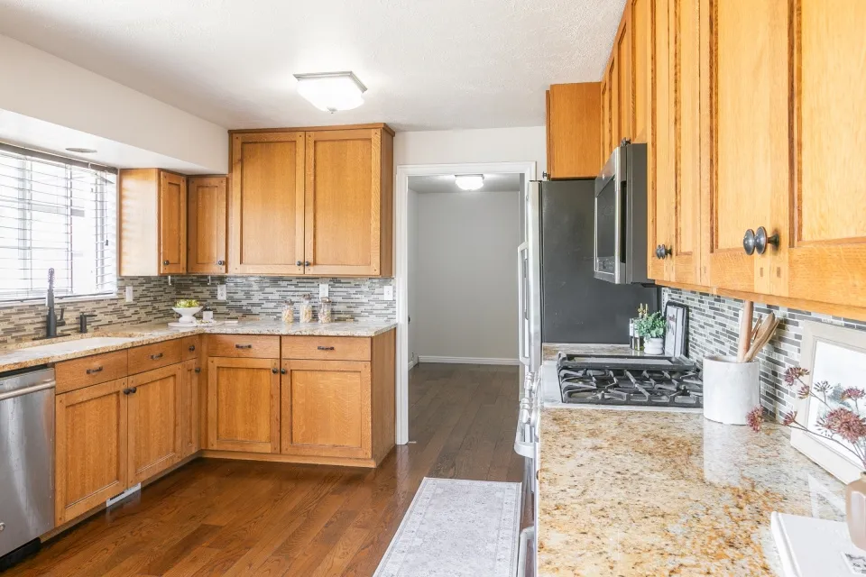 Kitchen featuring wood-finish cabinetry, granite-style countertops, a mosaic tile backsplash, stainless steel dishwasher, and a built-in microwave above the range