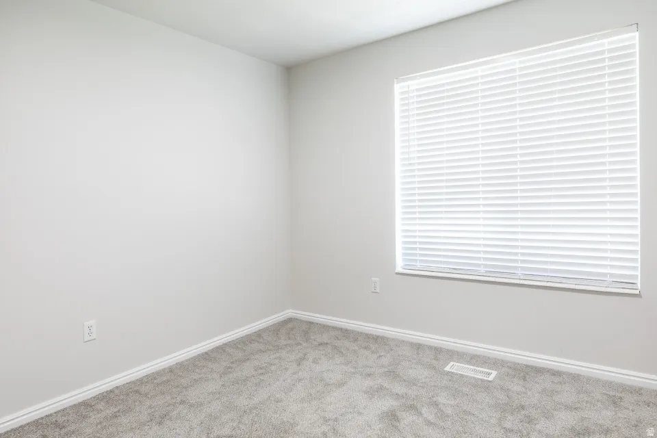 Spacious room with light gray wall paint, gray carpet flooring, and a large window with horizontal blinds