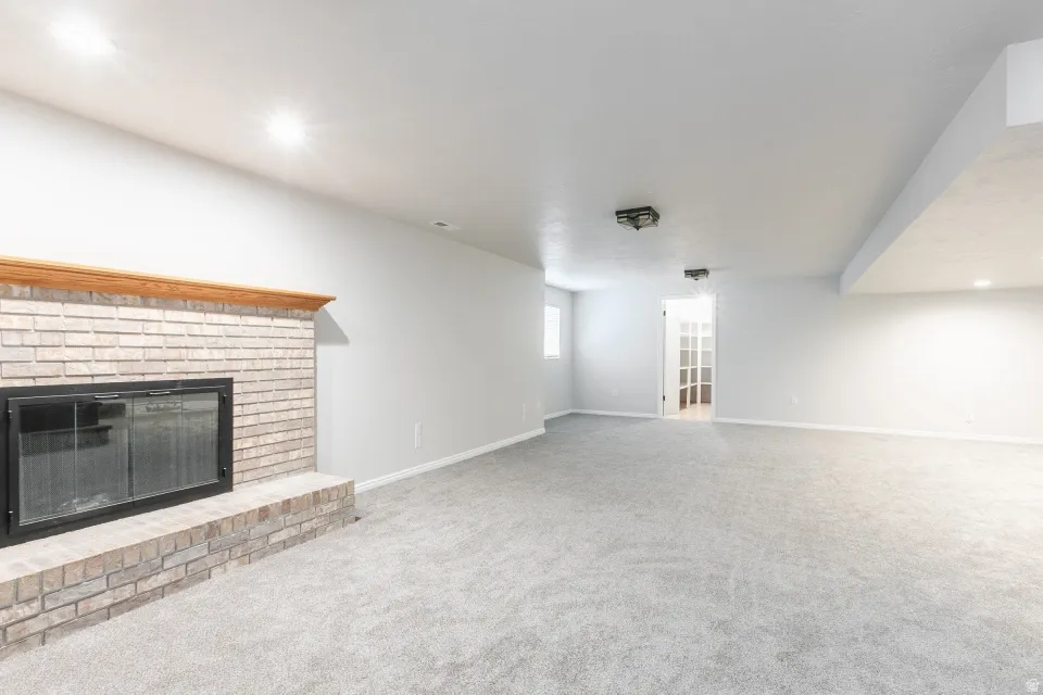 Spacious room featuring a light-colored brick fireplace with a wood mantel, light gray carpet, recessed lighting, and a white French door