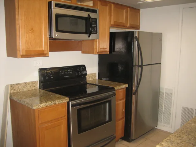 Kitchen featuring natural wood cabinetry, granite countertops, and stainless steel appliances including an over-the-range microwave