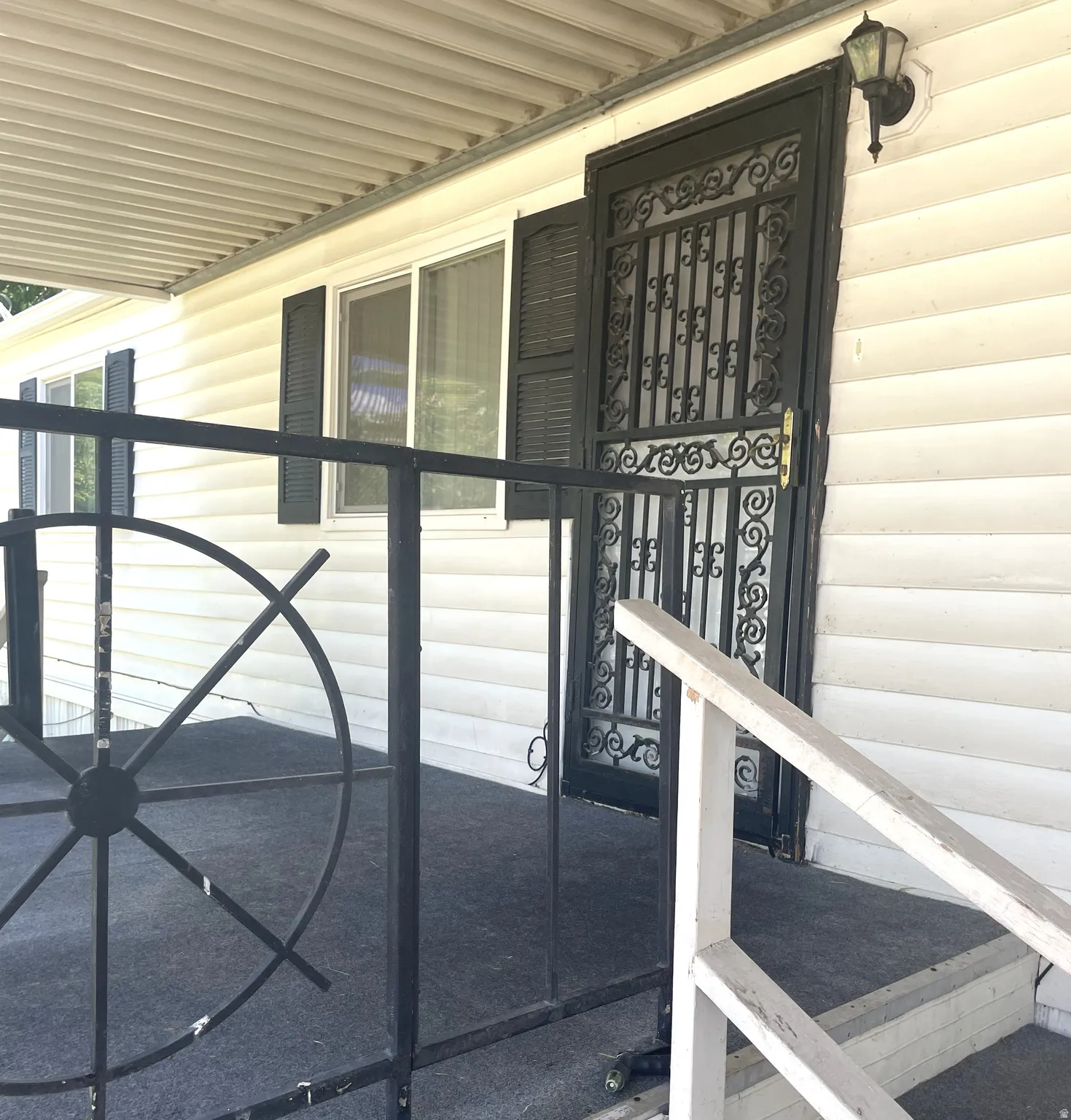 Front porch featuring a decorative black metal security door, dual-pane windows with louvered shutters, and a covered patio area