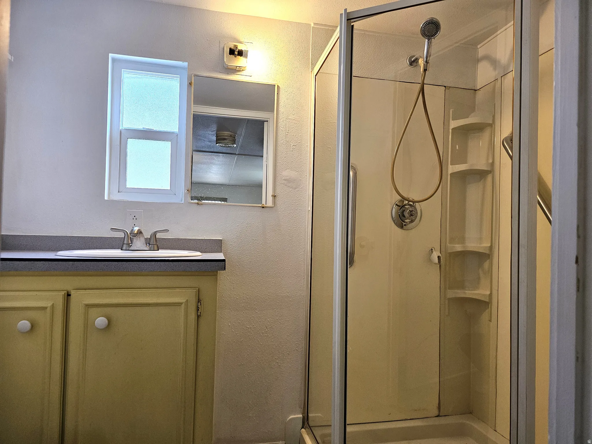 Bathroom featuring a glass-enclosed shower, single vanity with integrated sink, window, wall-mounted light fixture, and mirrored medicine cabinet