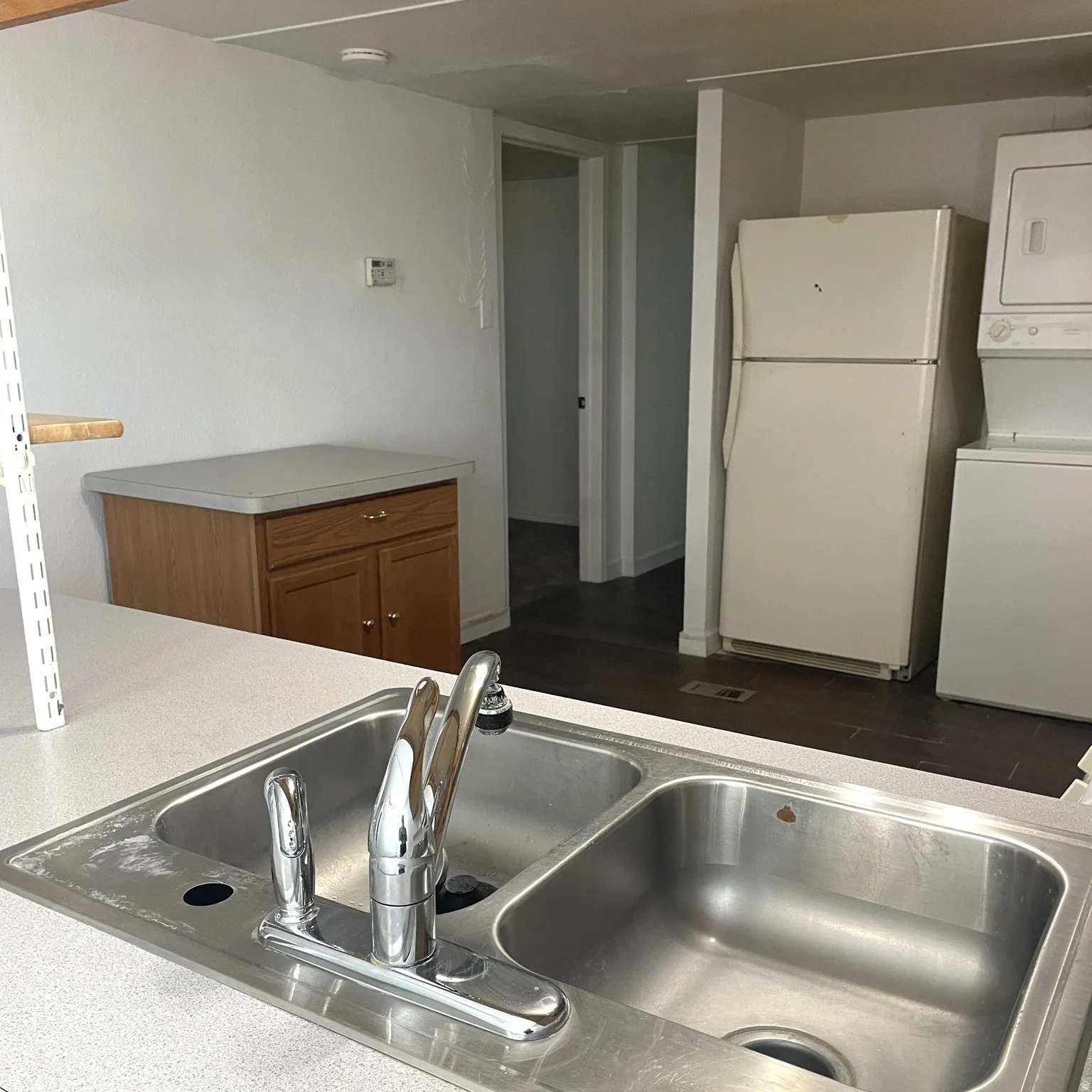 Kitchen area with a double basin stainless steel sink, chrome faucet, and white laminate countertops