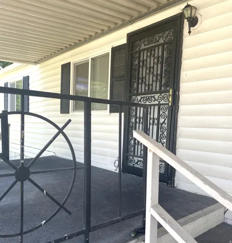 Front porch featuring a decorative black metal security door, dual-pane windows with louvered shutters, and a covered patio area