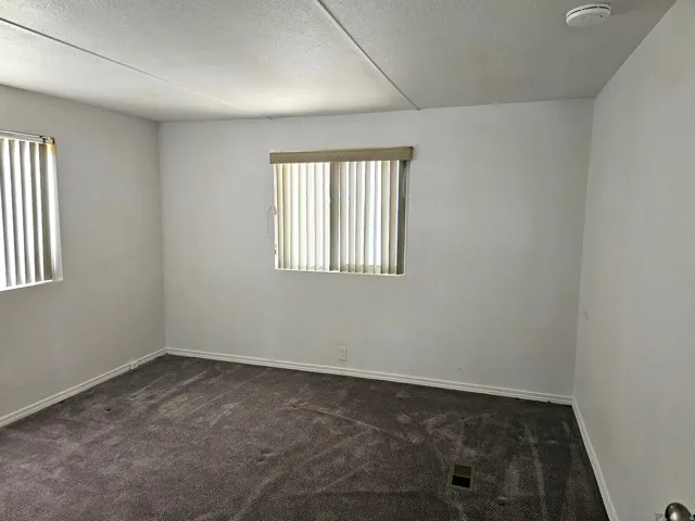 Carpeted room with white walls, two windows featuring vertical blinds, and a white smoke detector on the ceiling