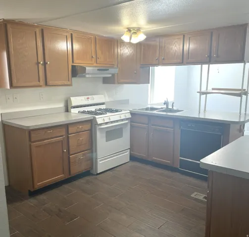Kitchen featuring wood-finish cabinetry, light-toned countertops, a gas range, dual basin sink, and tile flooring