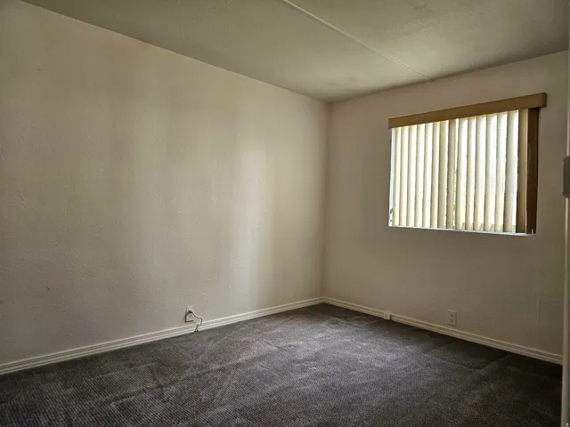 Room featuring textured white walls, a single window with vertical blinds, baseboard molding, and dark gray carpet flooring