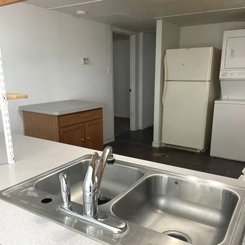 Kitchen area with a double basin stainless steel sink, chrome faucet, and white laminate countertops