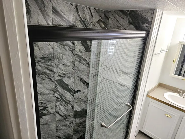Shower enclosure featuring patterned glass doors with a metal handle, dark-toned frame, and a wall-mounted showerhead