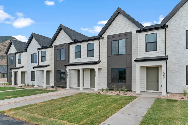 Modern townhome exterior featuring contemporary siding, dark-framed windows, a covered entry, and a mountain backdrop