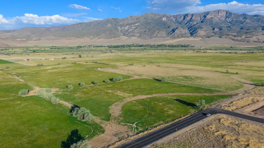 Expansive green acreage featuring a paved road, scattered mature trees, and distant mountain backdrops