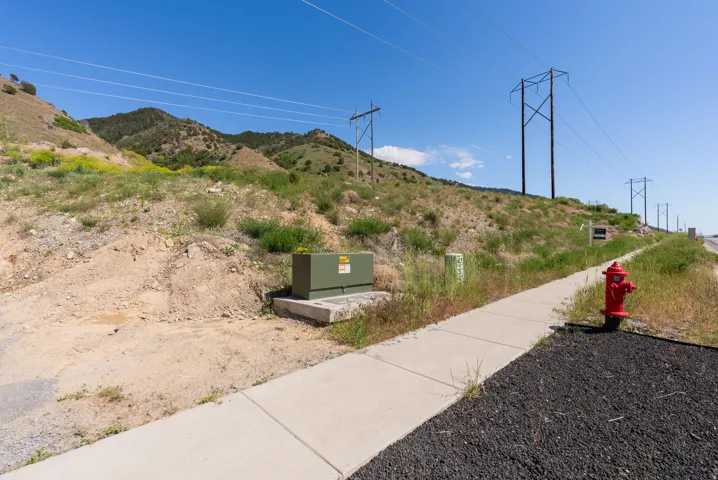Mountainous terrain with a clear sky, featuring a paved sidewalk, fire hydrant, and utility box