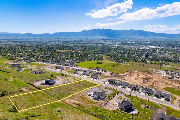 Expansive undeveloped lot with a natural grass and scrub landscape, offering a broad panorama of distant mountains and a valley with established residential areas