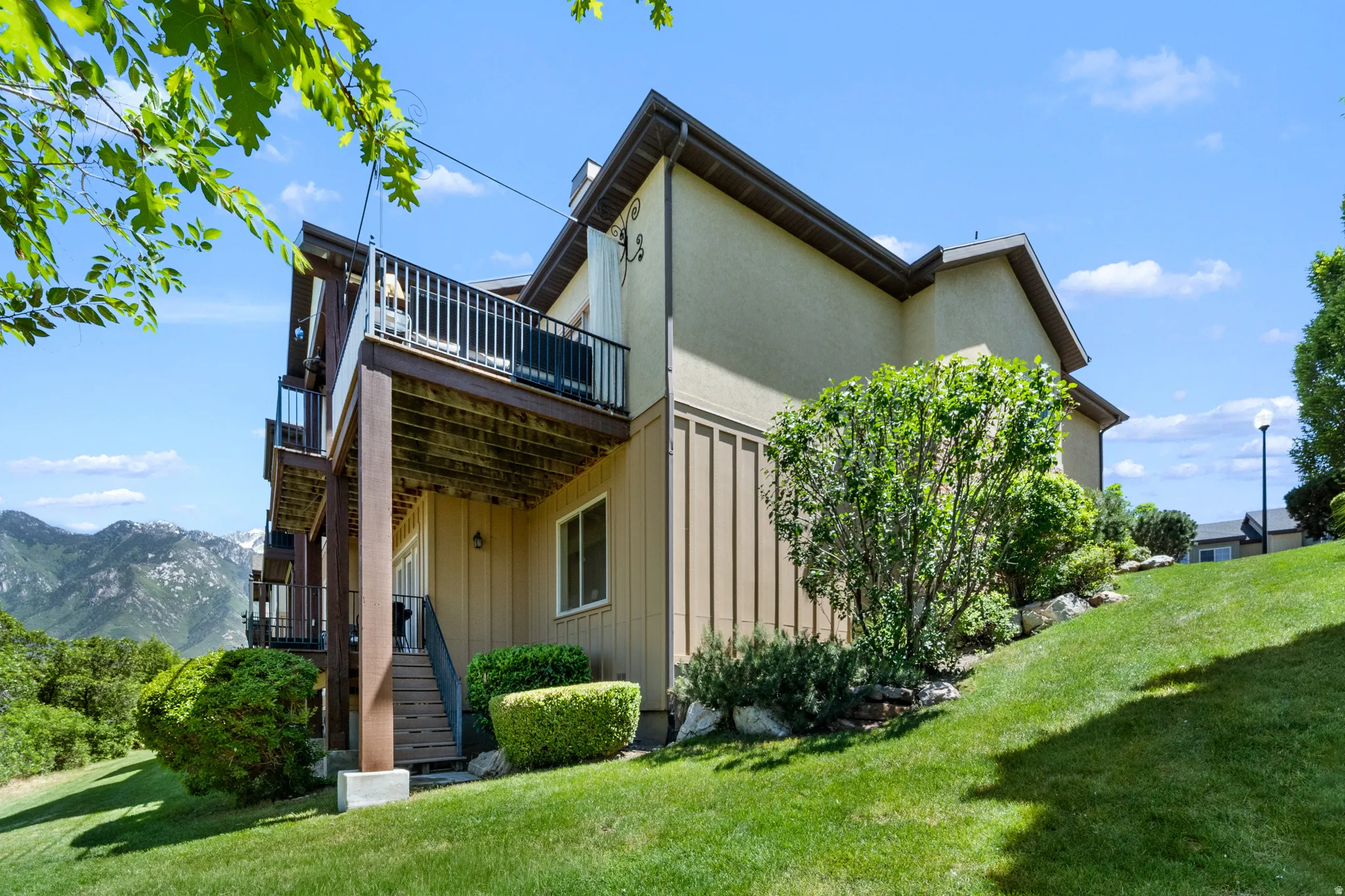 Terraced property featuring multiple balconies with metal railings, a stucco exterior, and a sloped, manicured lawn with established landscaping
