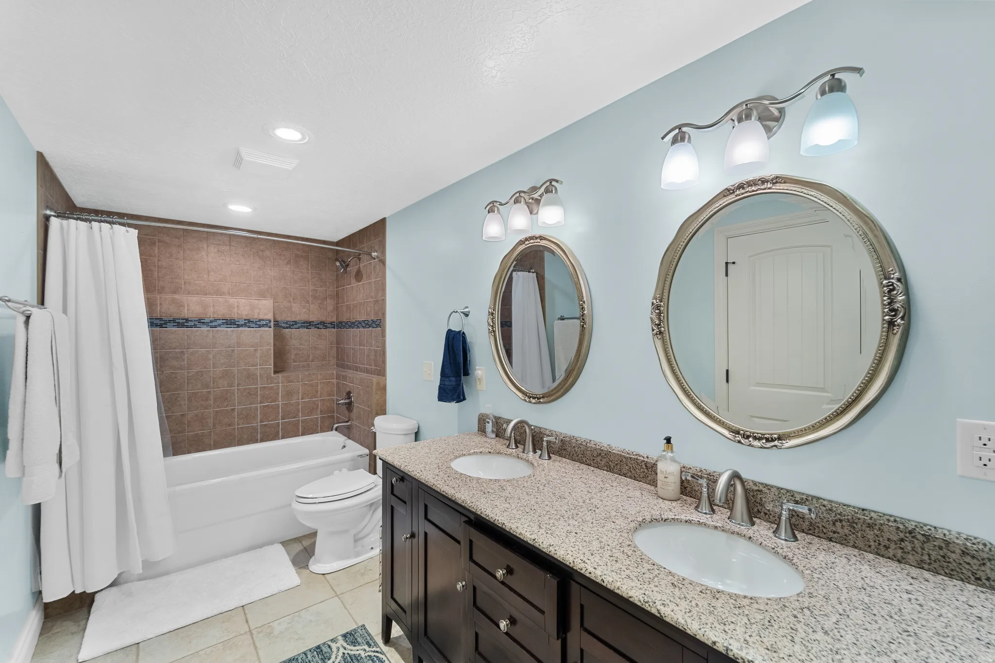 Double vanity featuring granite-look countertops, undermount sinks, and framed oval mirrors